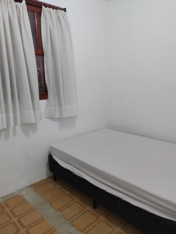 Cama en habitación con cortinas blancas en Chacara lima, en Pedro de Toledo