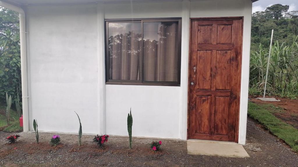 uma casa branca com uma porta de madeira e algumas flores em Hospedaje MV em Coto Brus