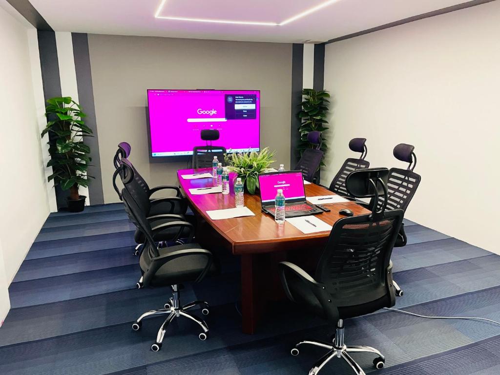 A shared meeting room set up with a central table, office chairs and a wall-mounted screen.