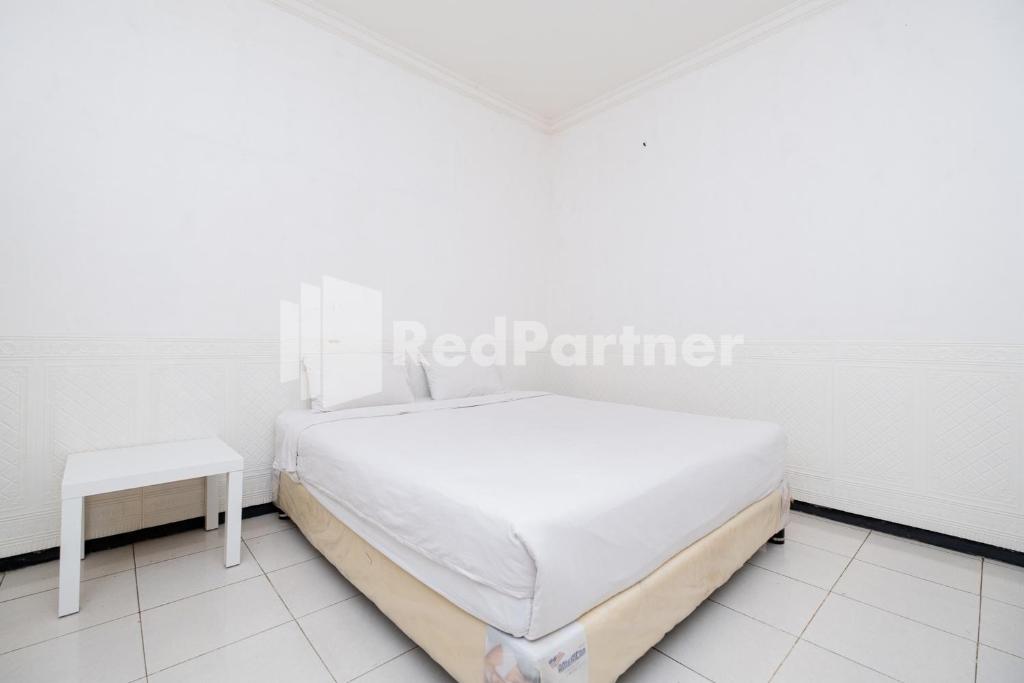 a white bedroom with a bed and a table at Dukuh Kupang Residence Mitra RedDoorz in Surabaya