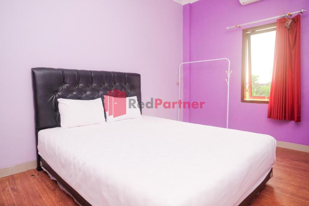 a bedroom with a large white bed with purple walls at Janna Guest House SYARIAH Yogyakarta Mitra RedDoorz in Yogyakarta
