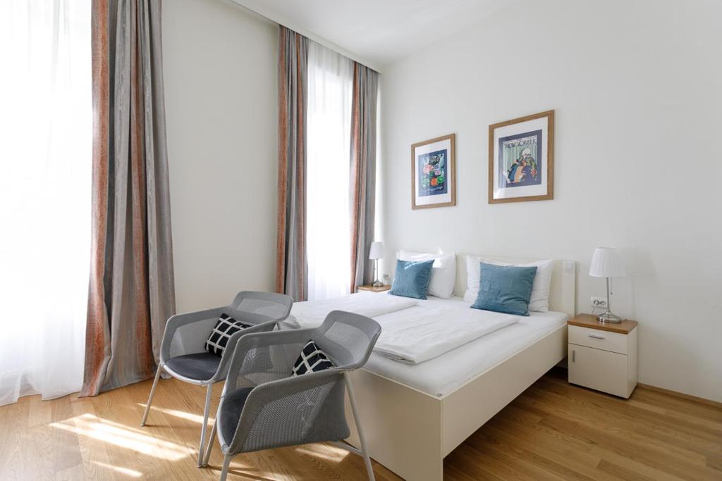 een witte slaapkamer met een bed en 2 stoelen bij Riess City Rooms - Self Check-in in Wenen