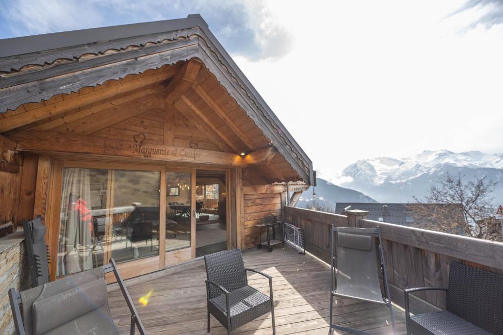 a wooden deck with chairs and a building with mountains at Beau chalet GUSTAVE 4 chambres 50m piste Huez Express in LʼHuez