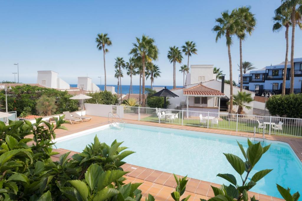 una piscina con palmeras y una casa en MAKĀI Bungalows, en Playa del Águila
