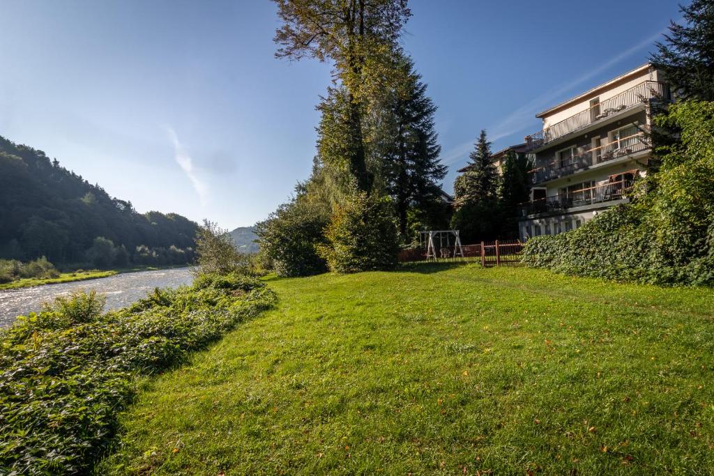 a grassy field next to a building next to a river at Apartamenty „Nad Popradem” in Rytro