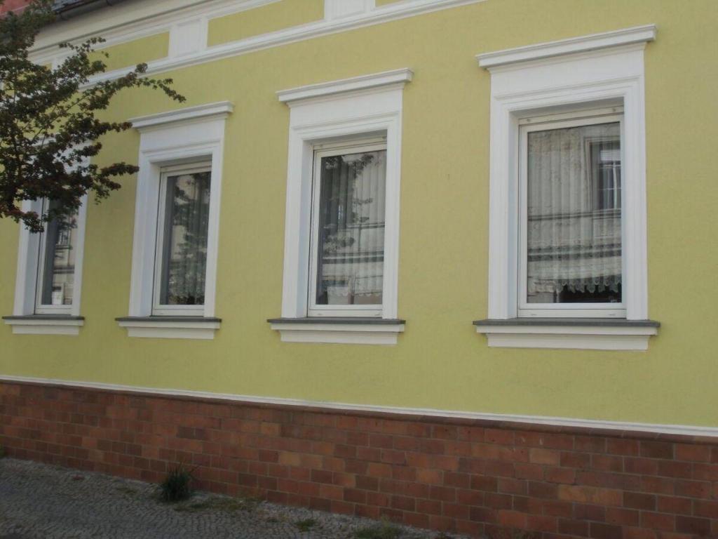 a yellow house with three windows and a brick wall at Ferienwohnung-Bille in Luckenwalde