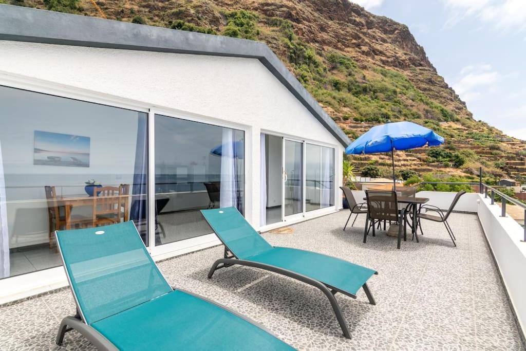 un patio con sedie, un tavolo e un ombrellone di Esterinha's Sunset Apartment by GALMI a Estreito da Calheta