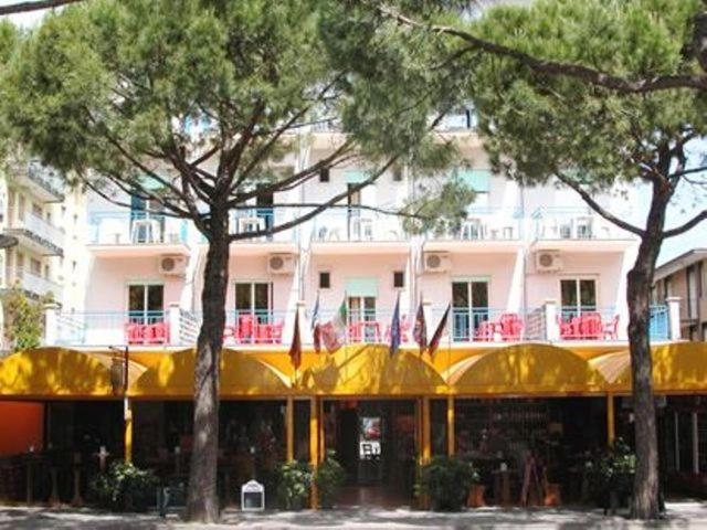 a building with a yellow roof and trees in front of it at Hotel Canova in Lido di Jesolo