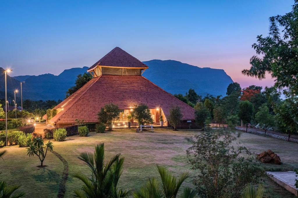 a large building in a field with mountains in the background at SaffronStays Satori Aves, Ultra Luxe Cottages On 8 Acres Estate, By The Mulshi Lake in Mulshi