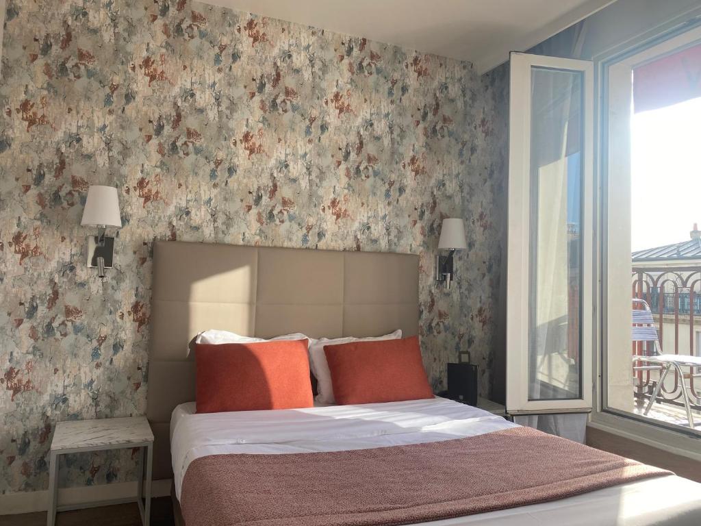 um quarto com uma cama com almofadas laranja e papel de parede floral em Hôtel De Venise em Paris