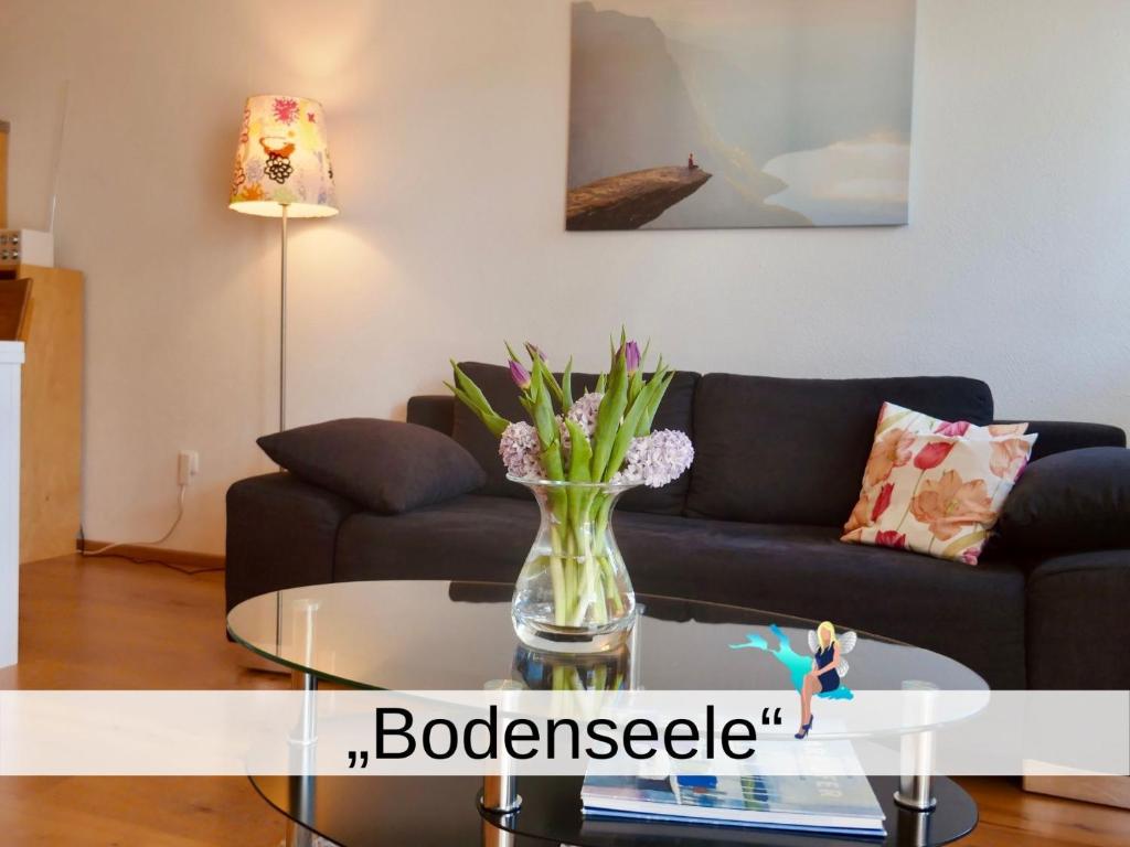 ein Wohnzimmer mit einem Sofa und einem Glastisch mit Blumen in der Unterkunft Ferienwohnung Bodenseele - Wohlfühloase mit großem Sonnenbalkon in Langenargen