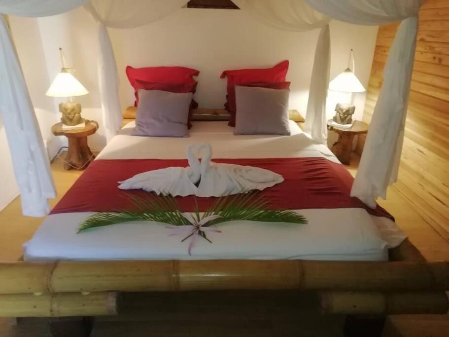 a bedroom with a large bed with red and white sheets at Bungalow atypique Ti Bambou à 500m de la plage in Sainte-Anne