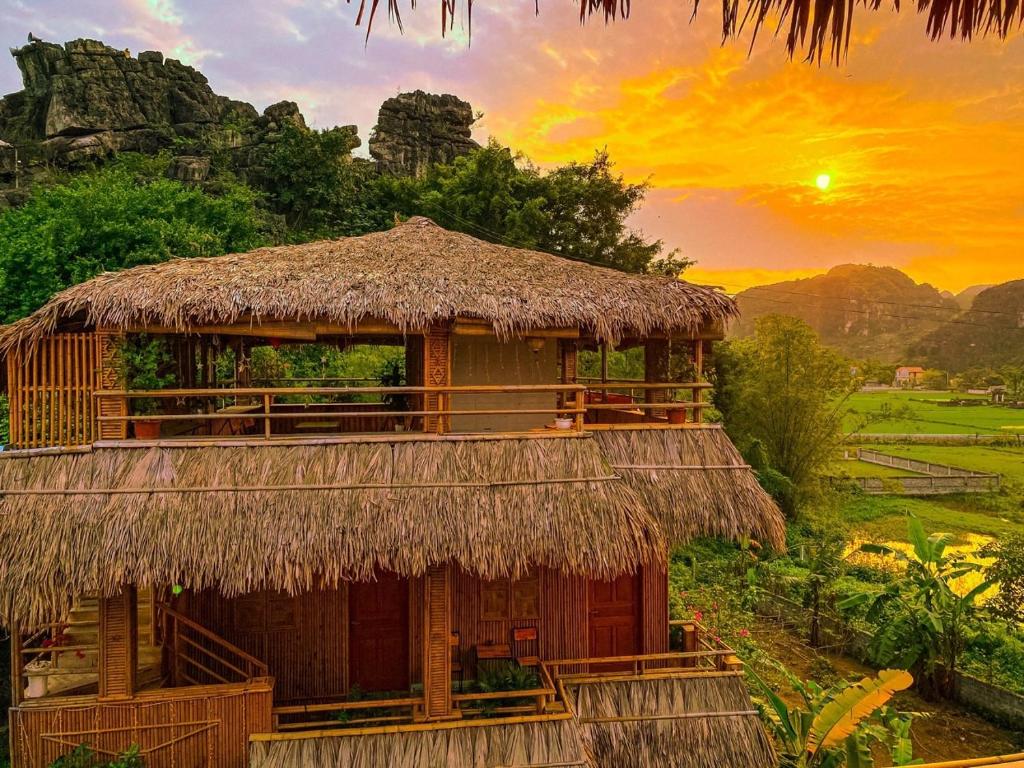 a hut with a straw roof with a sunset in the background at Hang Mua Bamboo Homestay Ninh Binh in Ninh Binh