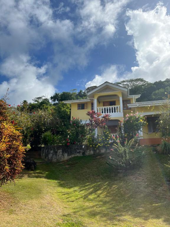 una casa amarilla con porche y algunos arbustos en Maison Marikel en Mahe