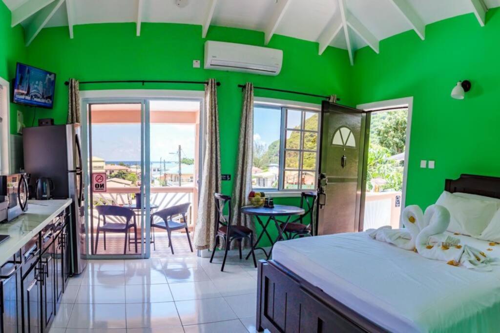 ein grünes Schlafzimmer mit einem Bett, einem Tisch und Stühlen in der Unterkunft Maggie's Inn in Soufrière