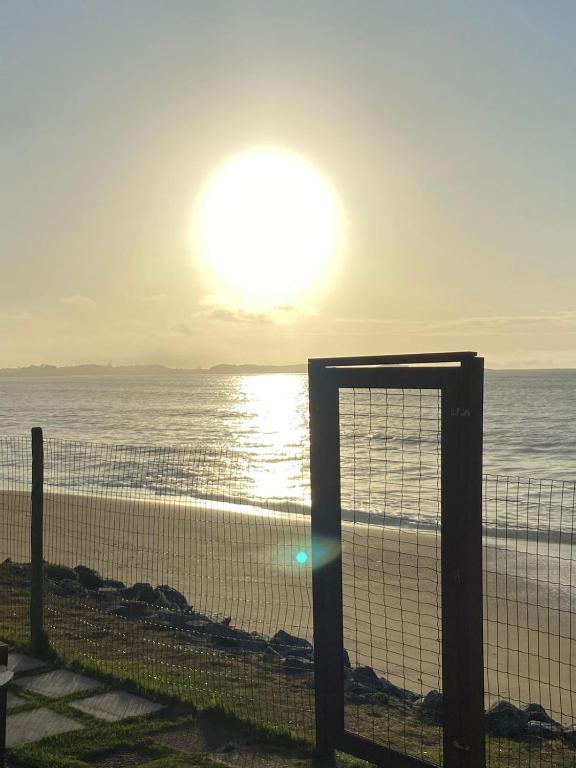 a fence on the beach with the sun in the sky at Casa de Praia PÉ NA AREIA em Rio das Ostras RJ in Rio das Ostras