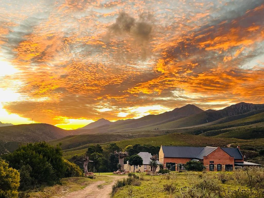 a house on a field with a sunset in the mountains at Old Farmhouse Cottage in Kareedouw