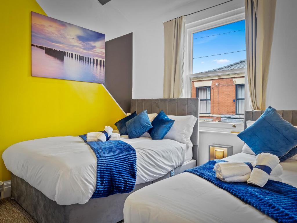 Preston Serviced Apartment - Estatevision في بريستون: غرفة نوم بسريرين مع وسائد زرقاء وبيضاء