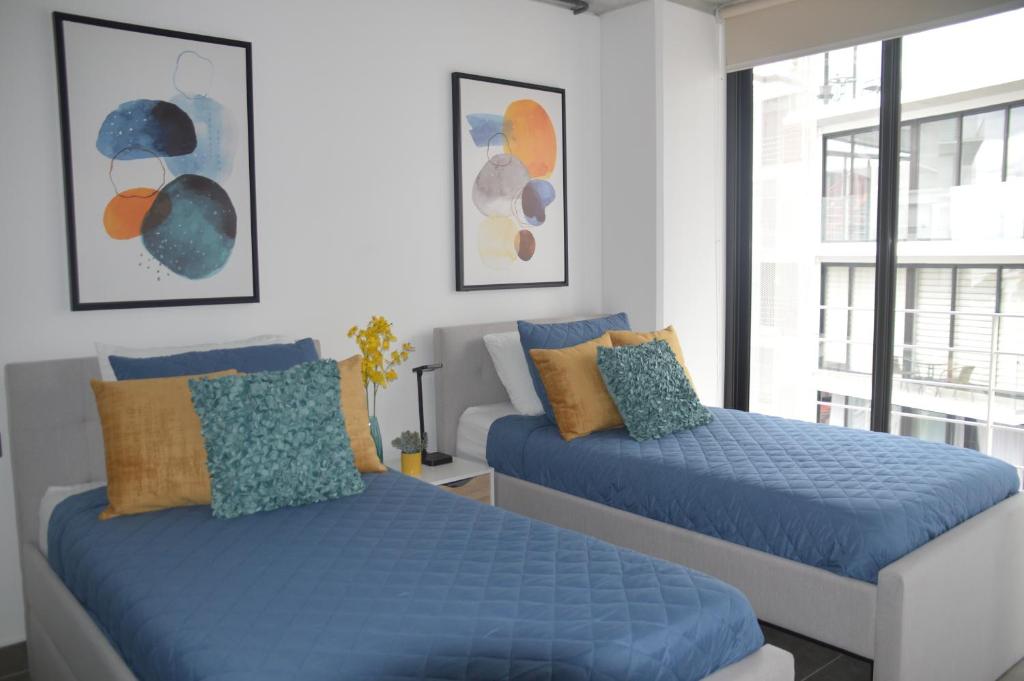 a bedroom with two blue beds and a window at Cozy Stays Cayala Apartments (401) in Guatemala