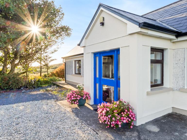 a house with a blue door and some flowers at Flaherty Cottage in Ballyconneely