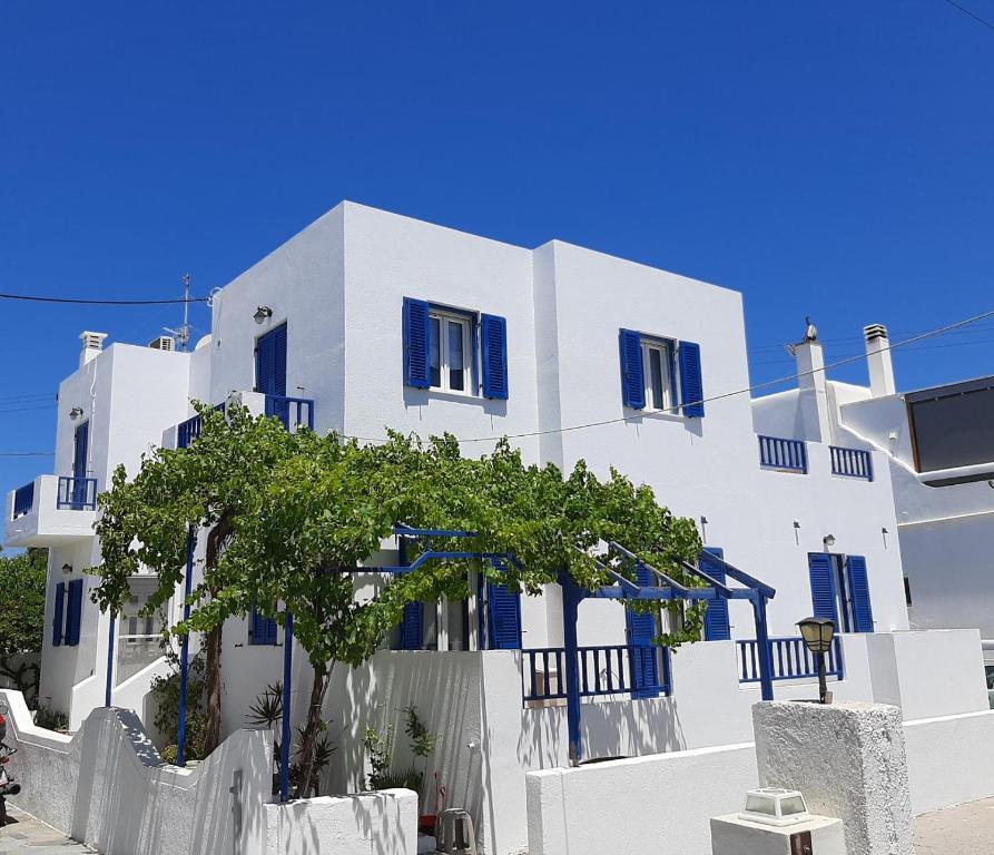 un bâtiment blanc avec des fenêtres bleues et un arbre devant dans l'établissement Sunshine apartment, à Adamas