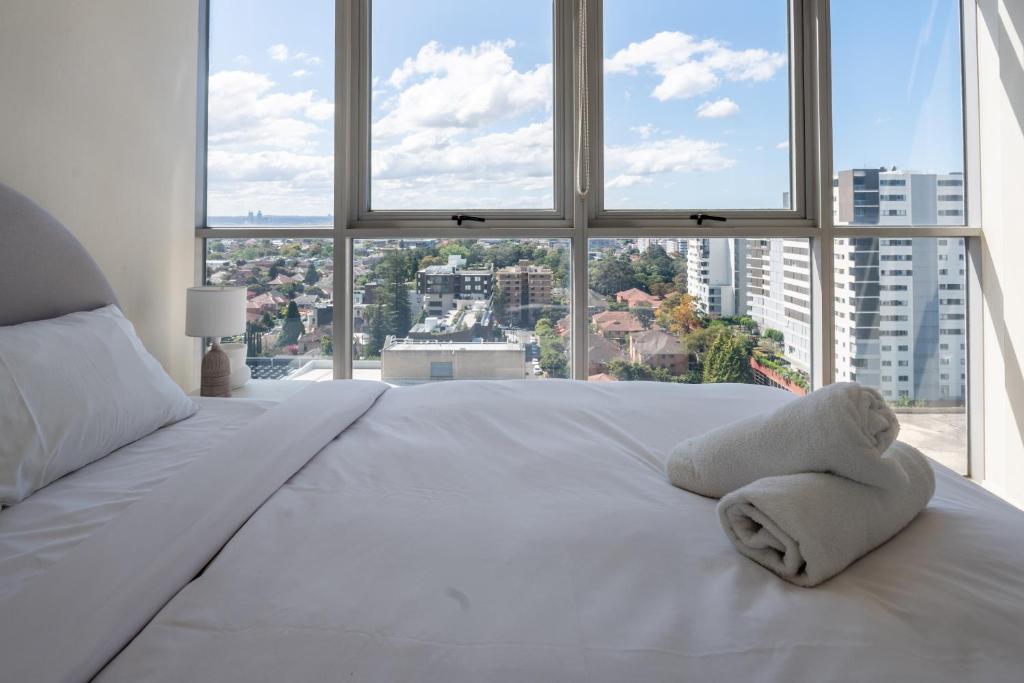 a white bed with a teddy bear on it in front of a window at Burwood 1bedroom Apartment next to Station in Sydney