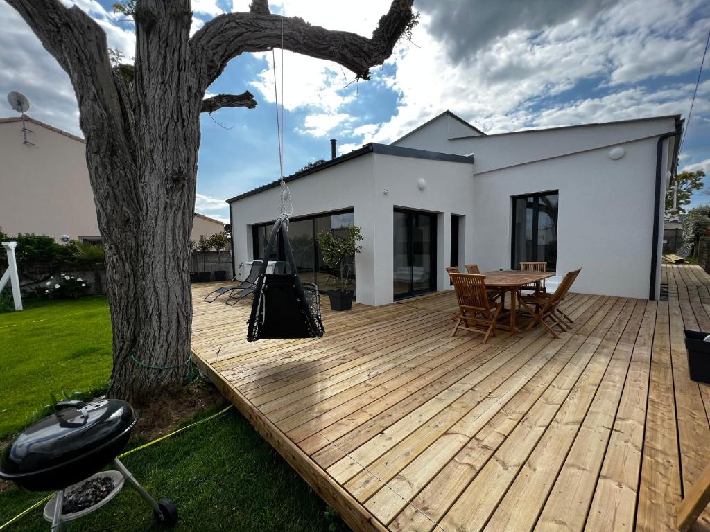 une terrasse en bois avec une table et un arbre dans l'établissement Villa Robinia Cormier 150 m de la plage, à La Plaine-sur-Mer
