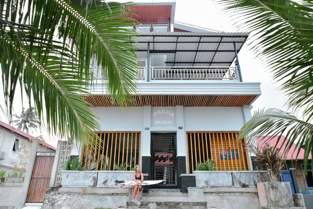 a woman sitting on the steps of a house with a surfboard at Oseda Nias Surf House in Hilibotodane