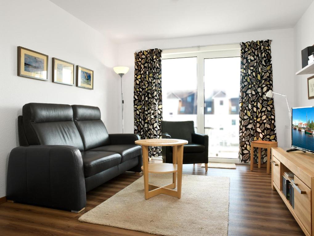 ein Wohnzimmer mit einem schwarzen Ledersofa und einem Tisch in der Unterkunft Residenz am Yachthafen Hornhecht in Kirchdorf