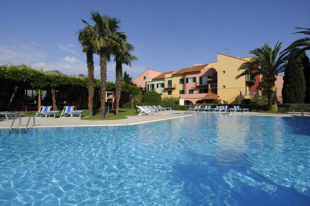 uma grande piscina com cadeiras e palmeiras em Residence i Cormorani em Loano