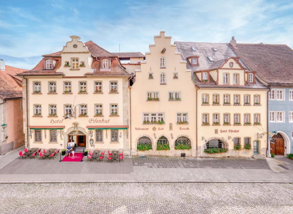 ein großes gelbes Gebäude mit roten Stühlen davor in der Unterkunft Hotel Eisenhut in Rothenburg ob der Tauber