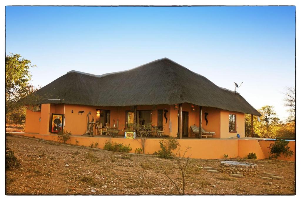 a large yellow house with a thatched roof at Yingwe self catering villa bordering Kruger with private pool in Phalaborwa