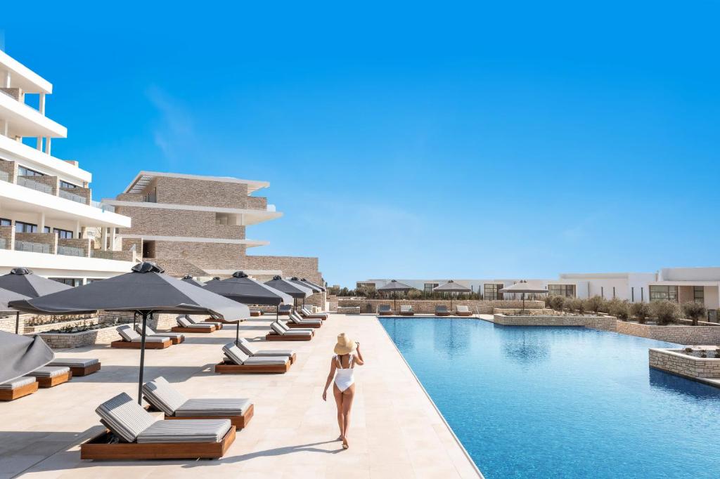 Una donna che cammina lungo la piscina in un resort di Cap St Georges Hotel & Resort a Peyia