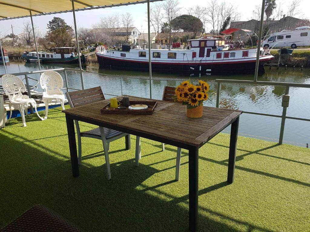 a wooden table with chairs and a boat in the water at PÉNICHE authentique tout confort in Aigues-Mortes