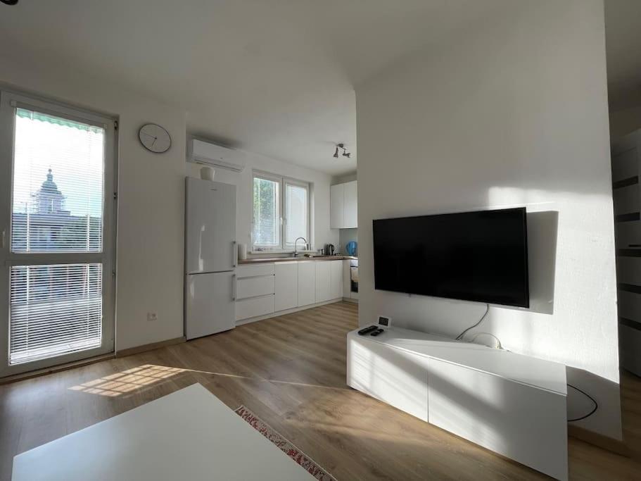 sala de estar blanca con TV de pantalla plana en la pared en New Stylish City Center Apartment, en Komárno