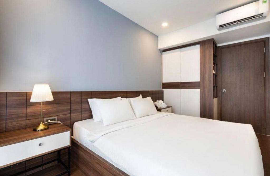 een slaapkamer met een wit bed en een nachtkastje met een lamp bij 2-bedroom Apartment with City View in District 7 in Ho Chi Minh-stad