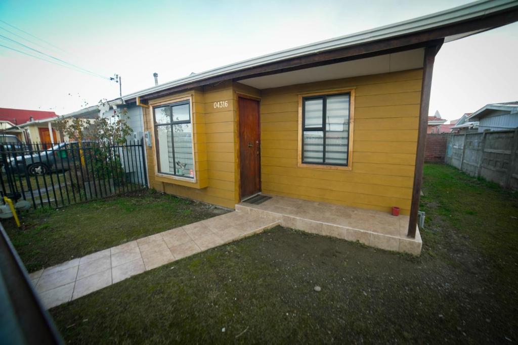 a small yellow house with a door on a yard at Departamento las Torres in Punta Arenas