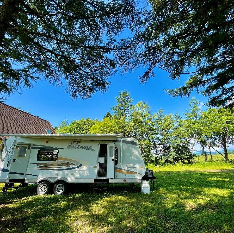 a camper parked in a field under a tree at ペンション 旅とPizzaとお宿 咲色-Sairo- in Nukabira