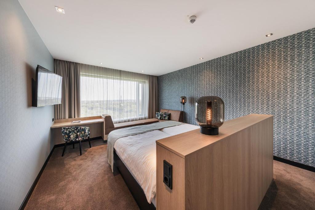 a bedroom with a bed and a desk and a window at Van der Valk Airporthotel Düsseldorf in Düsseldorf