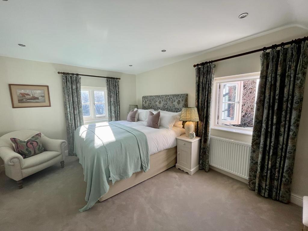 a bedroom with a bed and a chair and windows at Mimosa Cottage in Farnham