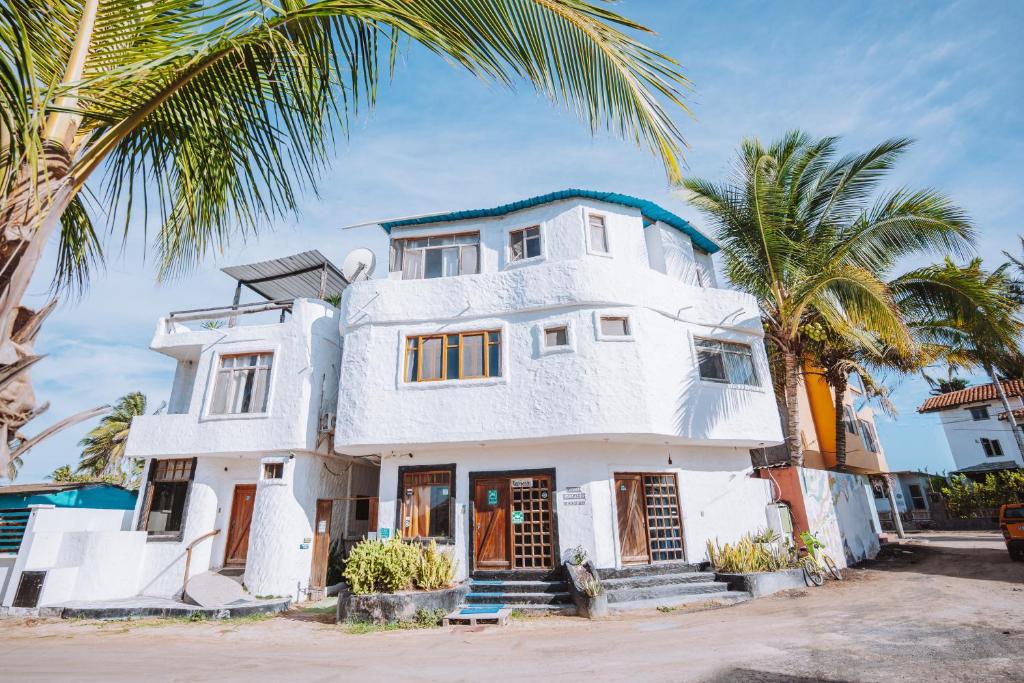 uma casa branca com palmeiras em frente em Hostal Galapagos by Bar de Beto em Puerto Villamil