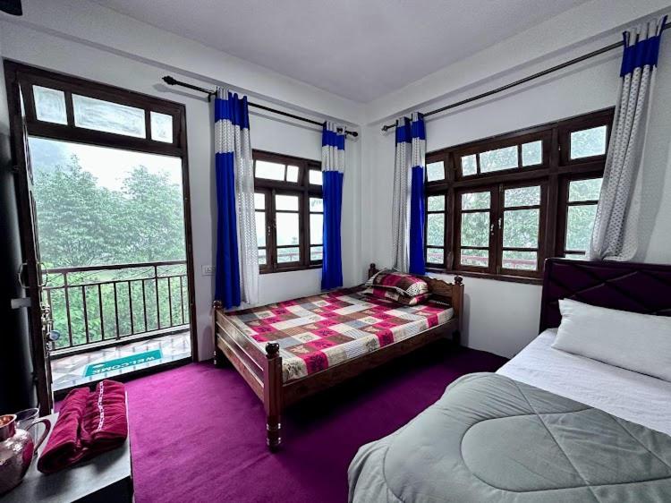 a bedroom with two beds and a balcony with windows at Syengden Nikunj in Darjeeling