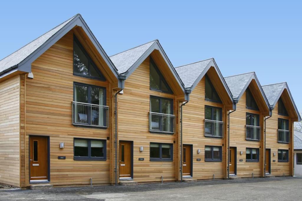 a row of wooden buildings with black roofs at Azalea Northbrook Park Chalet in Farnham