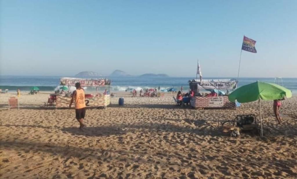 Un uomo in piedi su una spiaggia con un ombrellone verde di Pousada & Hostel Mar dos Ingleses a Florianópolis