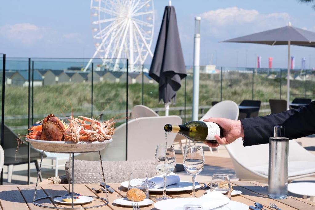 a man pouring wine into a table with a plate of food at Thalazur Ouistreham - Hôtel & Spa in Ouistreham