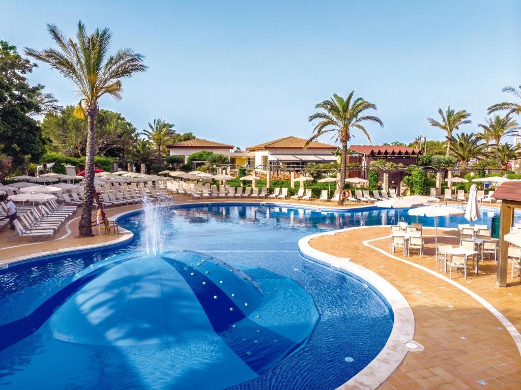 una piscina en un complejo con palmeras y sillas en Zafiro Menorca, en Cala'n Bosch