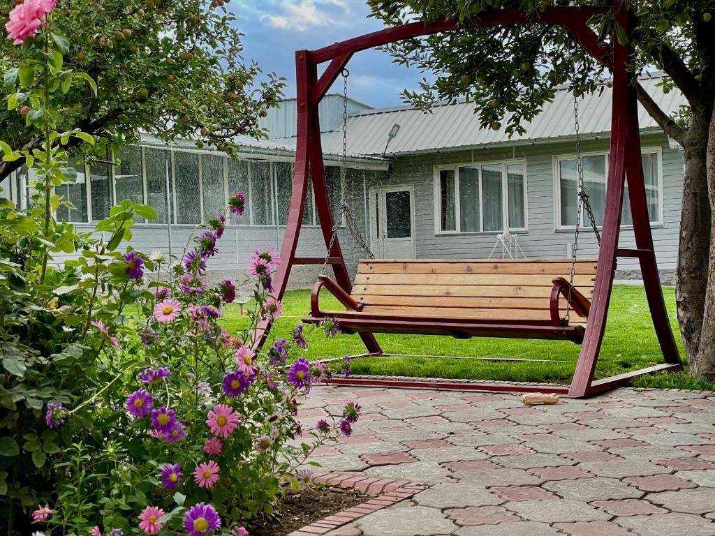 a wooden swing in front of a house with flowers at Sunny Valley Karakol in Karakol