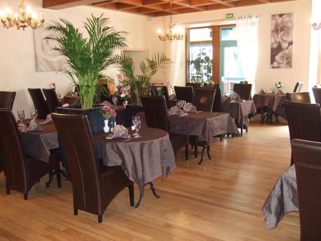 a dining room with tables and chairs and plants at Logis L'Ecu De France in Mauriac