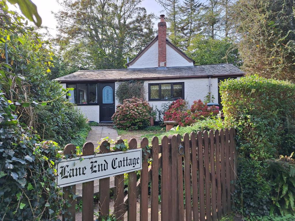 a small house behind a wooden fence with a sign at Lane End Cottage in Honiton