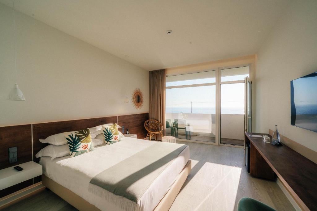 a hotel room with a bed and a large window at Porto Covo Praia Hotel & SPA in Porto Covo